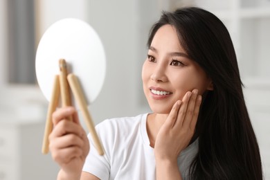 Woman with perfect skin looking at mirror indoors