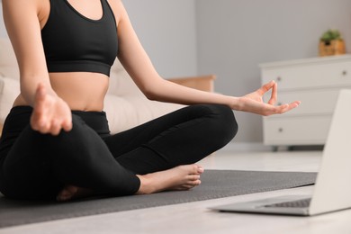 Photo of Woman practicing Padmasana with laptop on yoga mat at home, closeup. Lotus pose