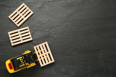 Photo of Toy forklift and wooden pallets on black table, flat lay. Space for text