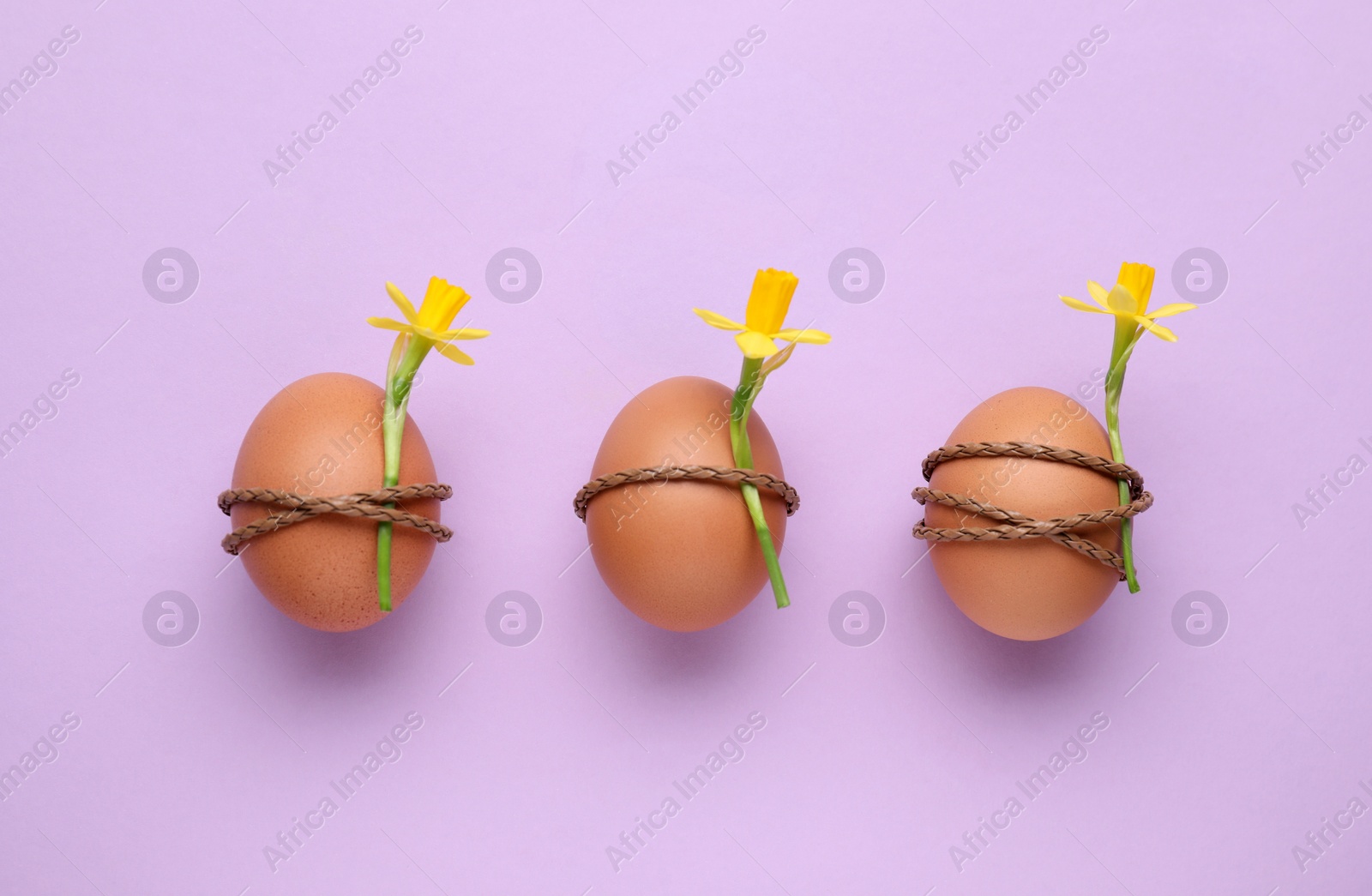 Photo of Easter eggs decorated with flowers on lilac background, top view