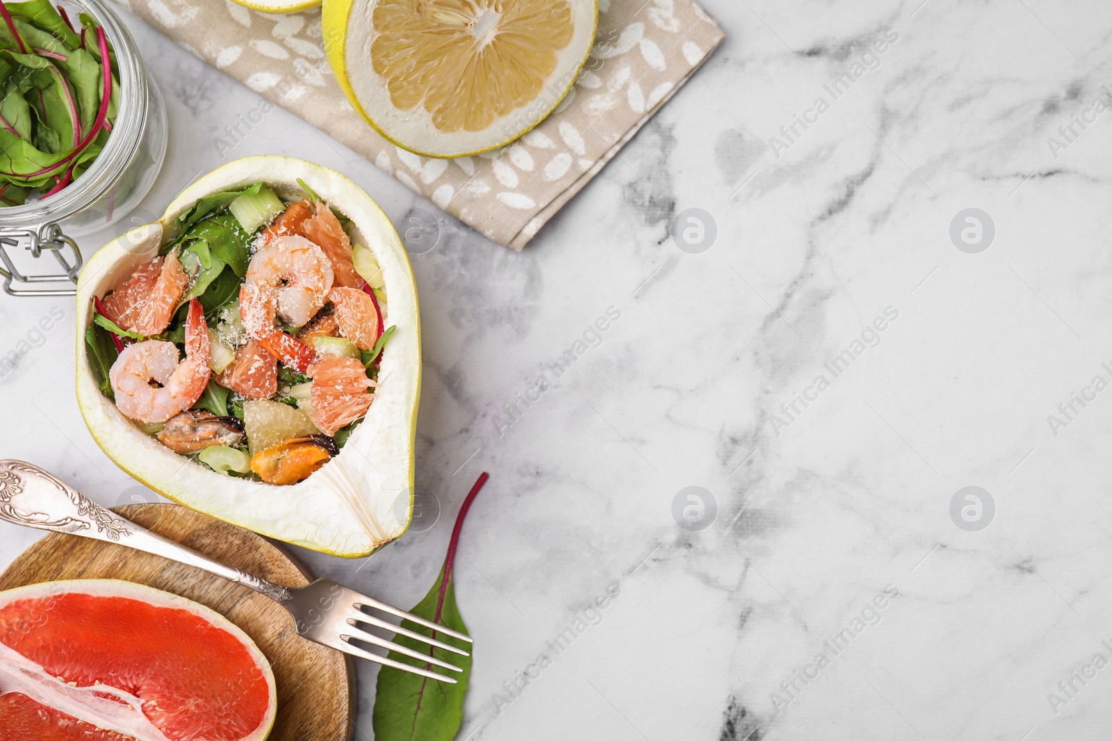 Photo of Delicious pomelo salad with shrimps in half of fruit on white marble table, flat lay. Space for text