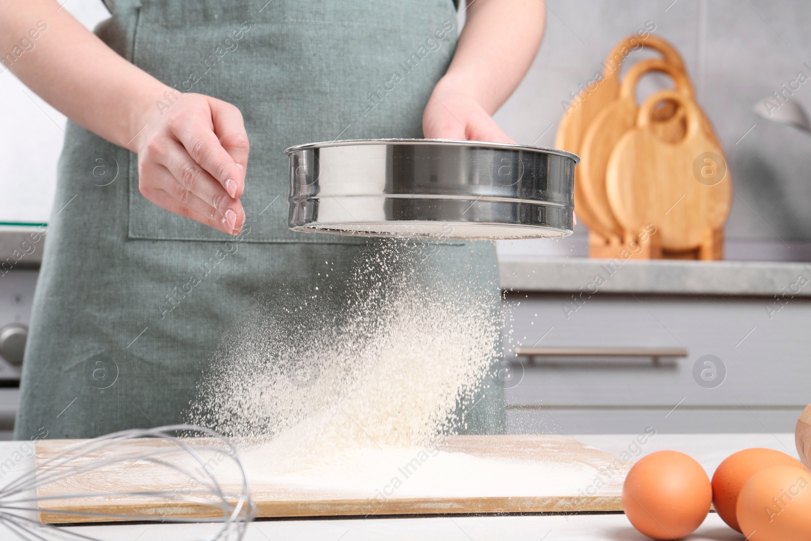 Photo of Woman sieving flour at table in kitchen, closeup