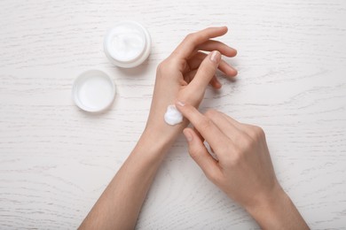 Woman applying body cream onto her wrist at white wooden table, top view