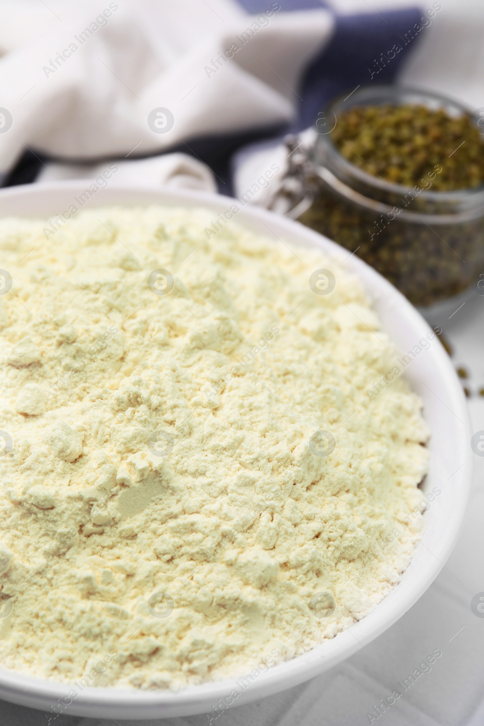 Photo of Mung bean flour in bowl and seeds on white tiled table, closeup