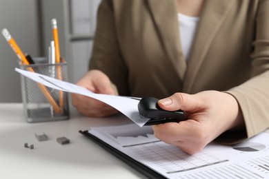 Photo of Woman with papers using stapler at white table indoors, closeup