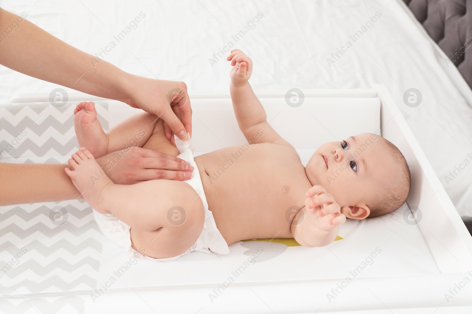 Photo of Mother changing her baby's diaper on table indoors