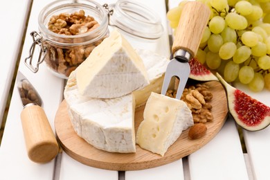 Delicious cheese, nuts and fruits on white wooden table