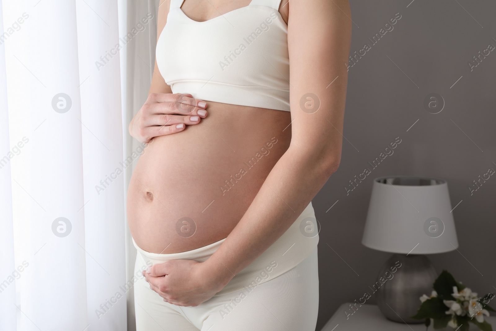 Photo of Pregnant woman near window at home, closeup