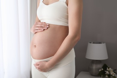 Pregnant woman near window at home, closeup
