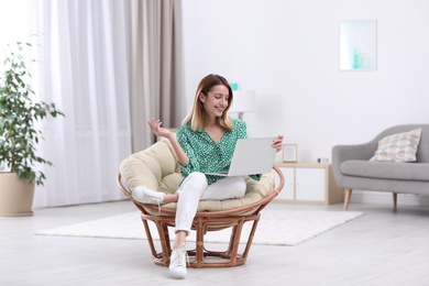 Attractive young woman with laptop in armchair at home