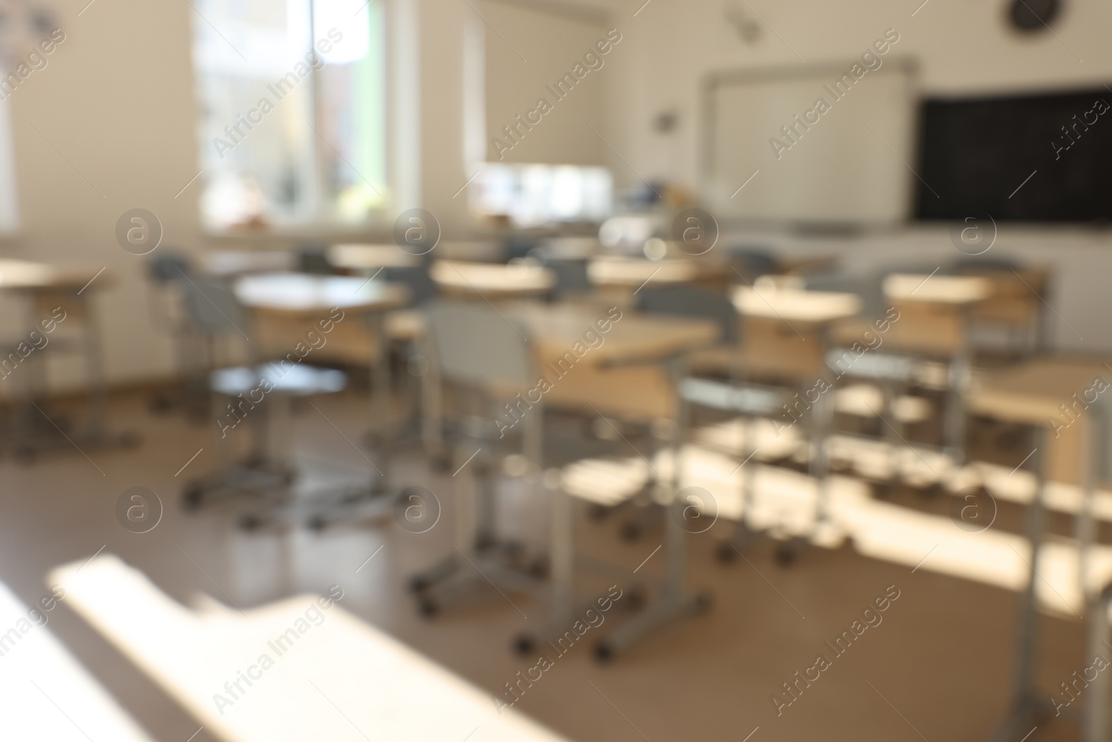 Photo of Blurred view of empty school classroom with desks, windows and chairs