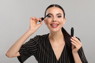 Photo of Everyday makeup. Beautiful woman applying mascara on light grey background