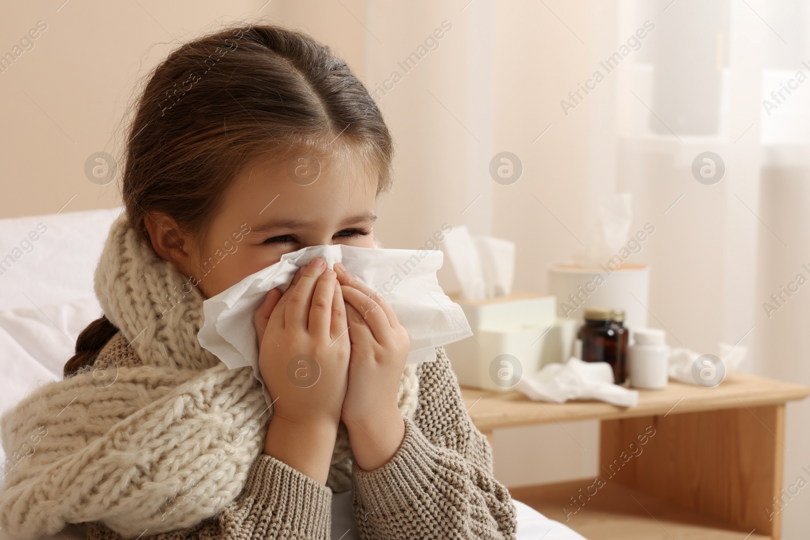 Photo of Girl blowing nose in tissue on bed in room. Cold symptoms