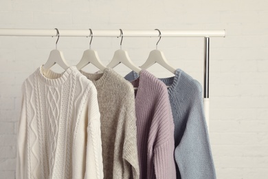 Collection of warm sweaters hanging on rack against white brick wall