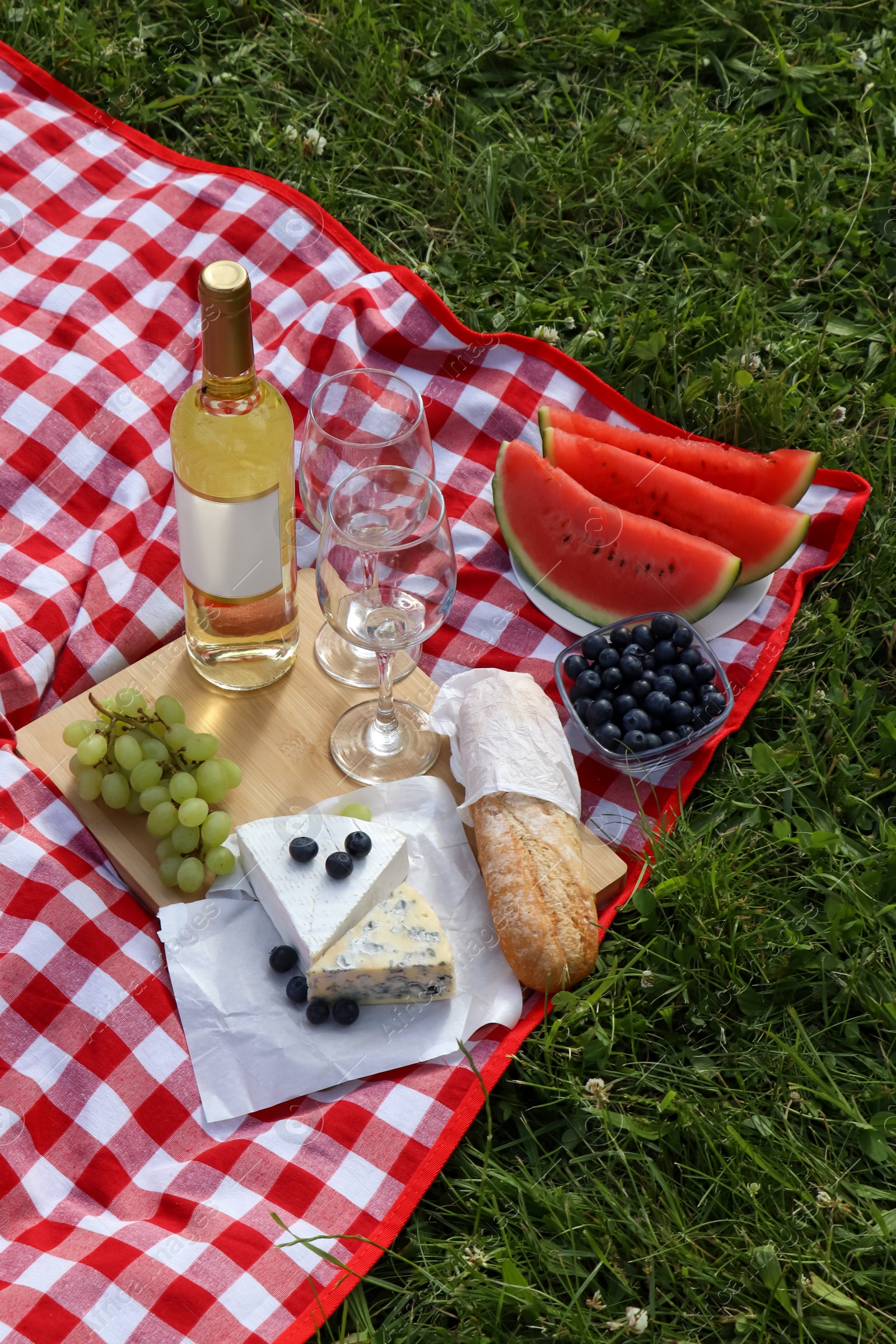 Photo of Picnic blanket with delicious food and wine outdoors on summer day