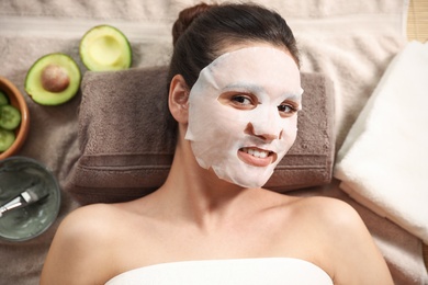 Woman with cotton mask sheet on face relaxing in spa salon, top view