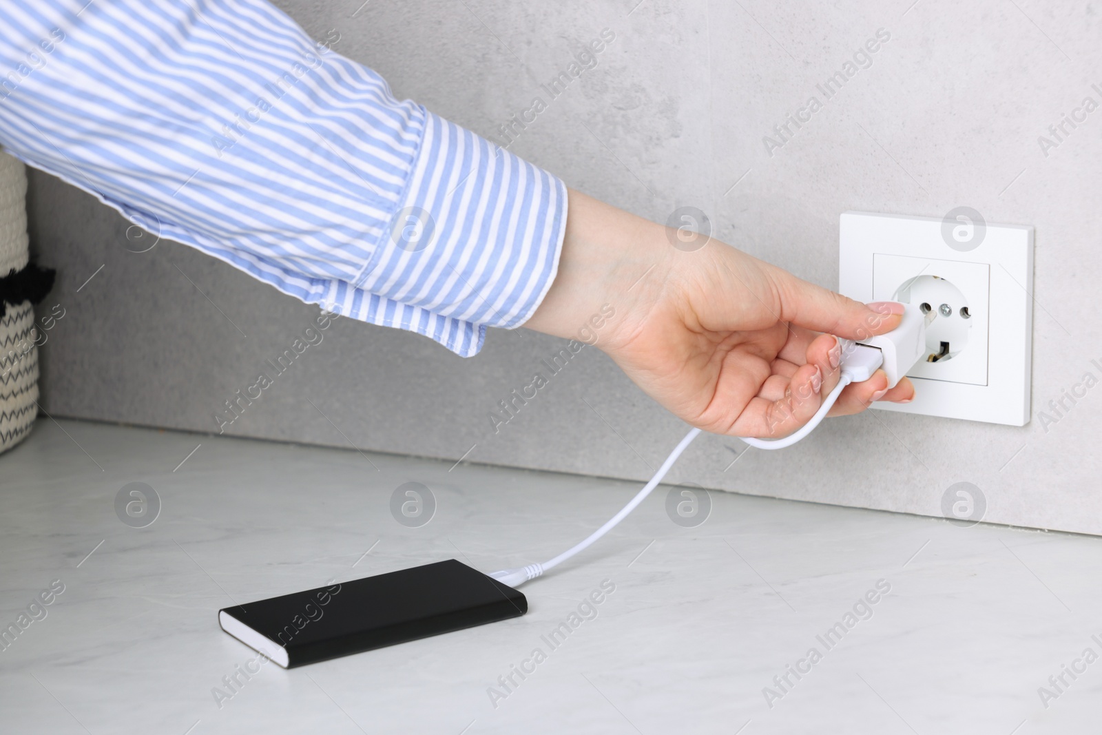 Photo of Woman plugging power bank into socket at white table indoors, closeup