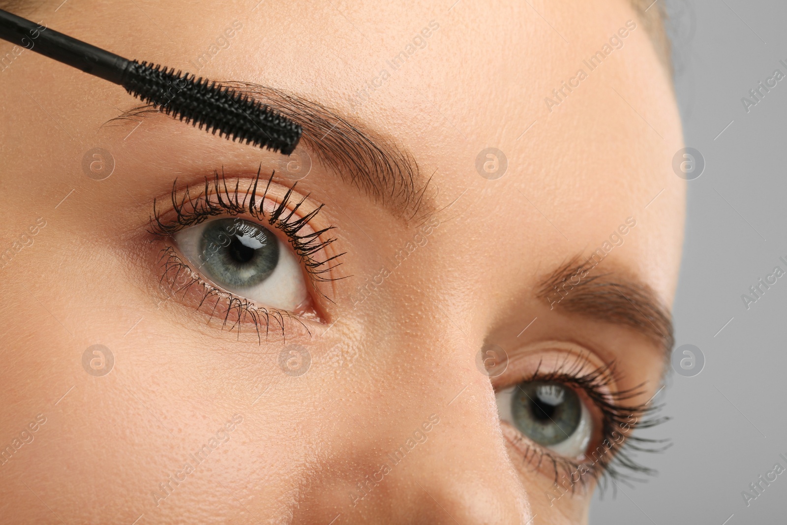 Photo of Woman applying mascara on grey background, closeup