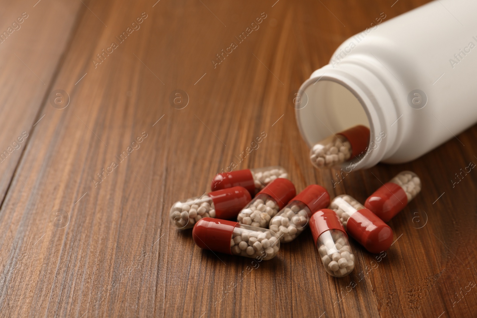 Photo of Overturned bottle with dietary supplement capsules on wooden table, closeup. Space for text