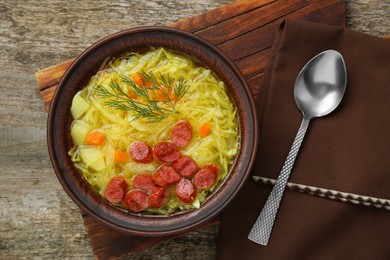 Photo of Delicious sauerkraut soup with smoked sausages and dill served on old wooden table, flat lay