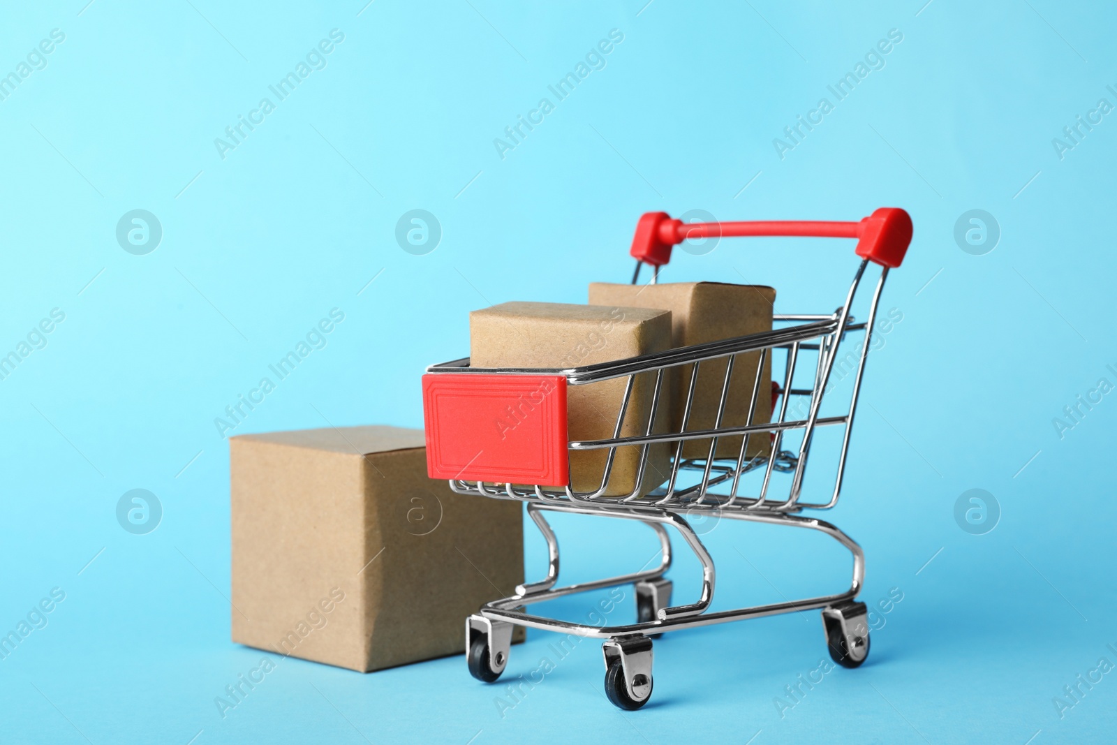 Photo of Shopping cart and boxes on light blue background. Logistics and wholesale concept