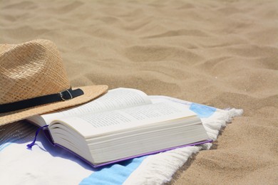 Photo of Beach towel with open book and straw hat on sand, space for text