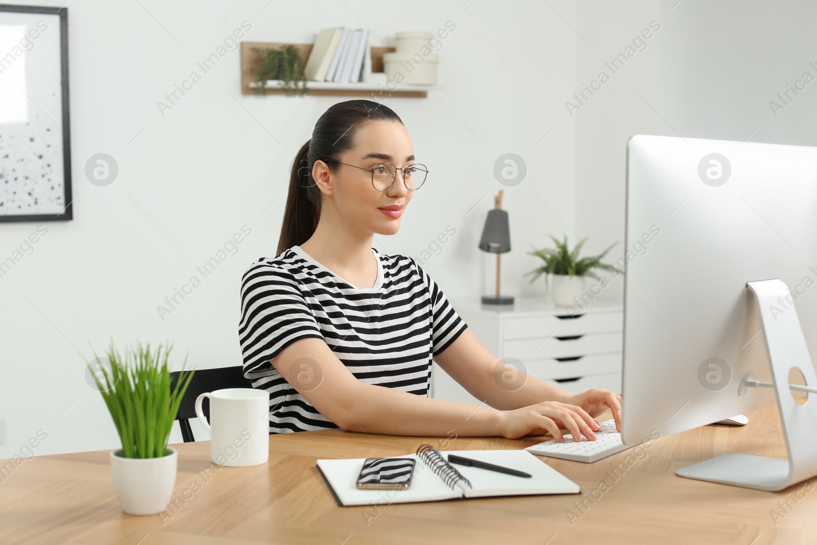 Photo of Home workplace. Woman working on computer at wooden desk in room