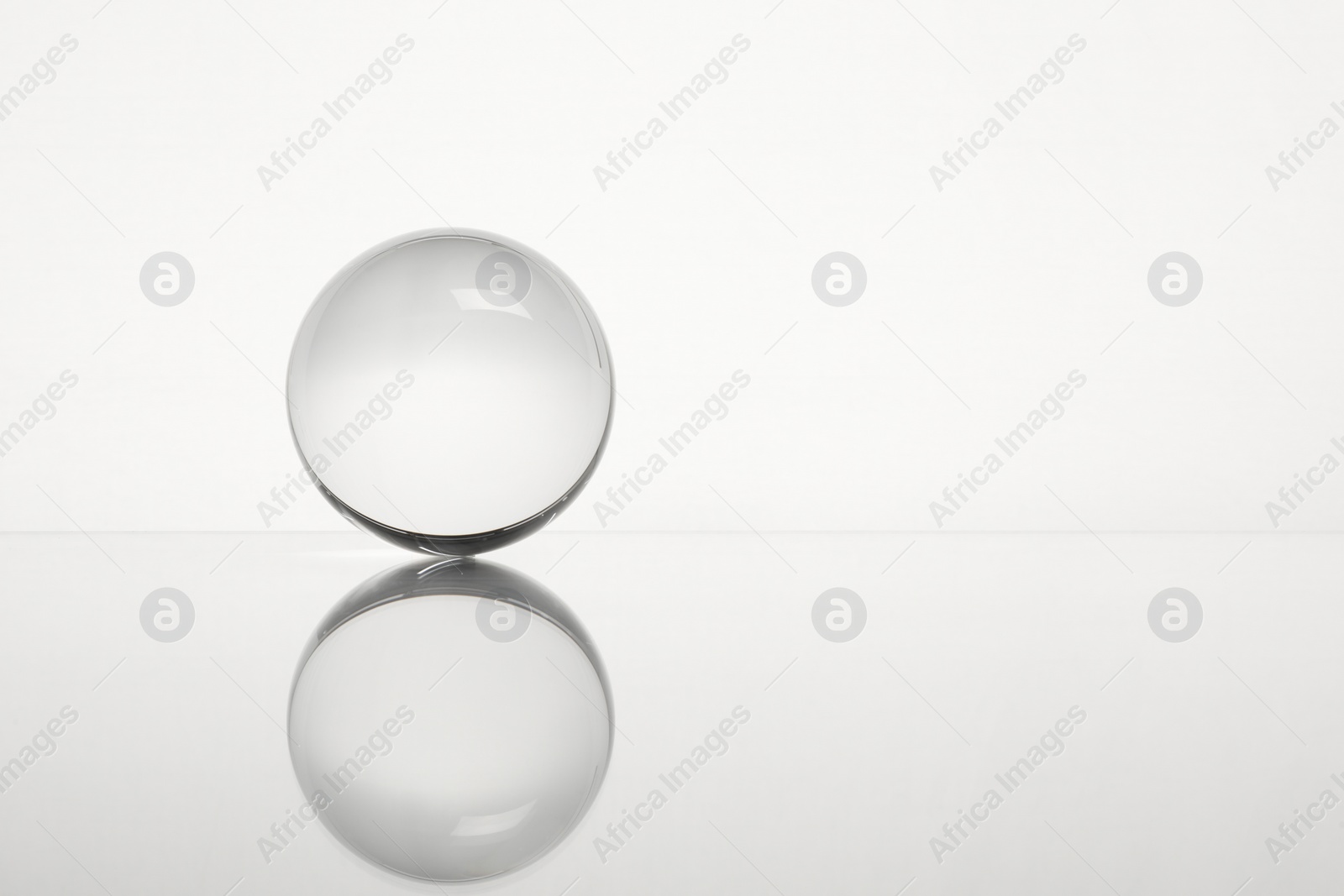 Photo of Transparent glass ball on mirror surface against white background. Space for text