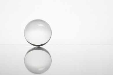 Photo of Transparent glass ball on mirror surface against white background. Space for text