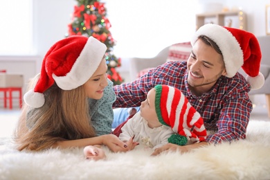 Photo of Happy couple with baby in Christmas hats at home