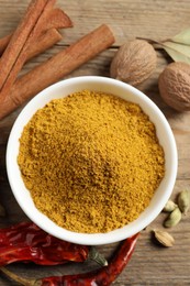 Photo of Dry curry powder in bowl and other spices on wooden table, flat lay