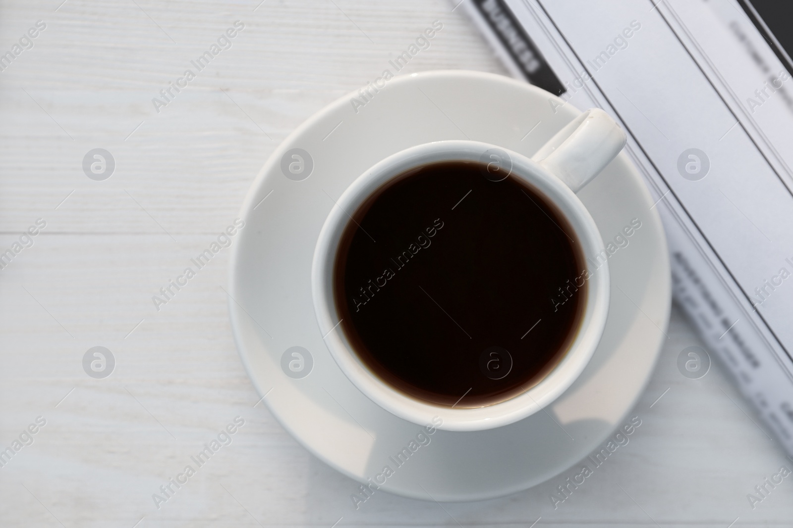 Photo of White cup with coffee and newspaper on wooden table in morning, flat lay