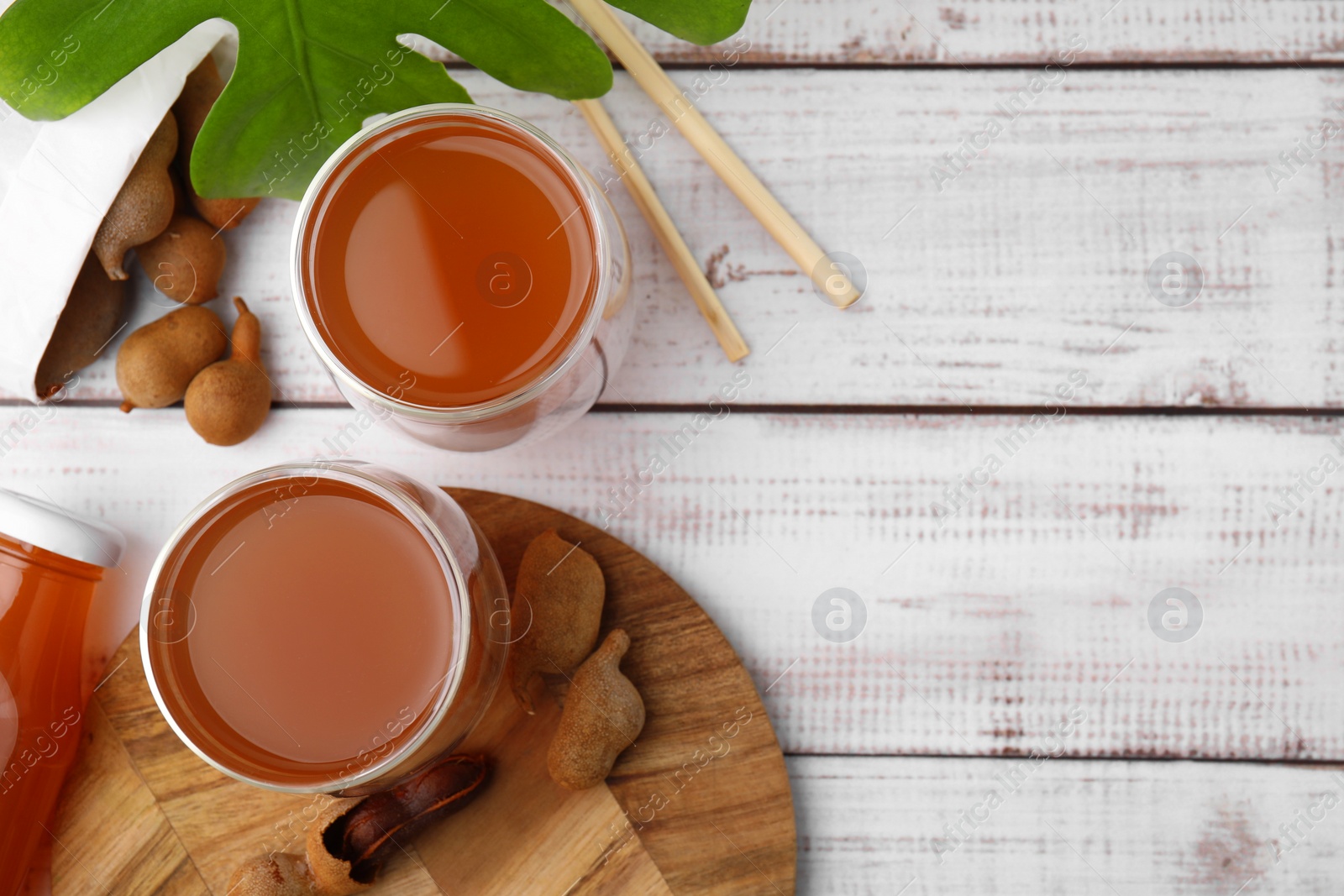 Photo of Tamarind juice and fresh fruits on white wooden table, flat lay. Space for text