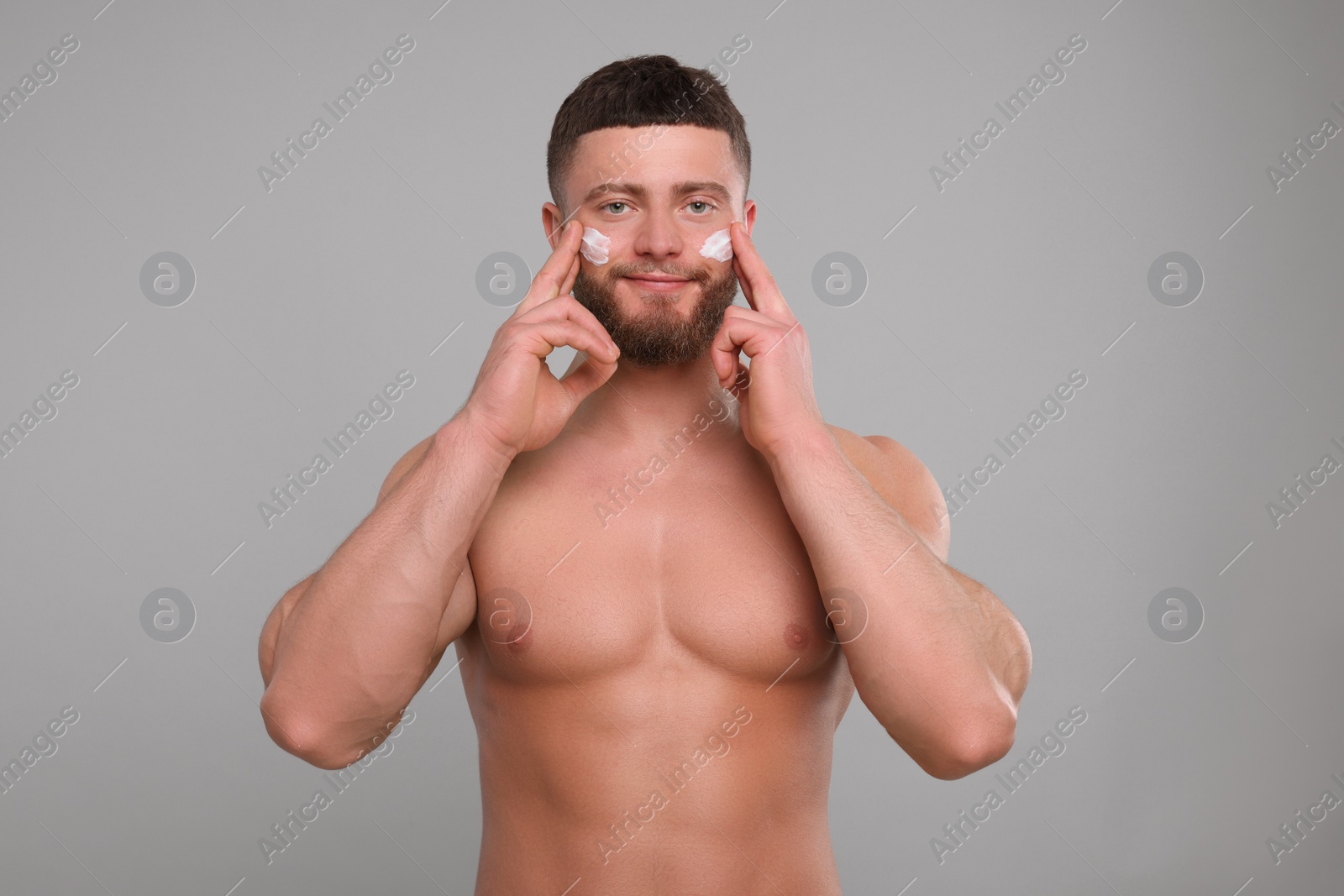 Photo of Handsome man applying cream onto his face on light grey background