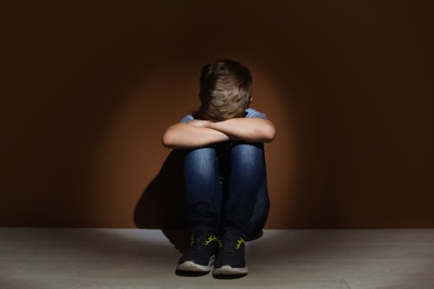 Photo of Depressed little boy sitting on floor indoors. Time to visit child psychologist