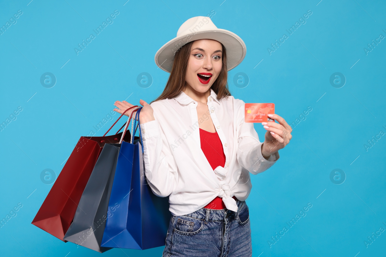 Photo of Excited young woman with shopping bags and credit card on light blue background