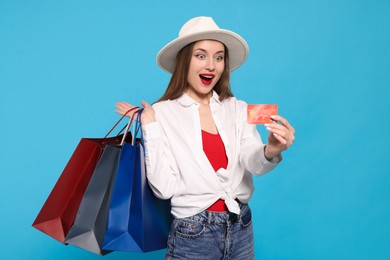 Photo of Excited young woman with shopping bags and credit card on light blue background