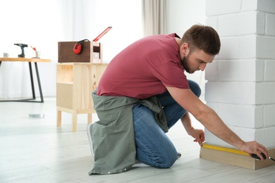 Photo of Young working man using measure tape at home, space for text