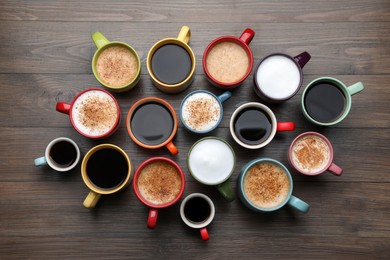 Many different cups with aromatic hot coffee on wooden table, flat lay