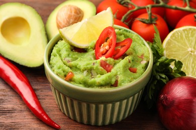 Photo of Bowl of delicious guacamole and ingredients on wooden table, closeup