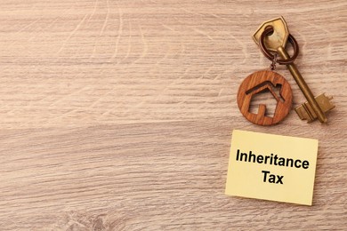 Photo of Inheritance Tax. Paper note and key with key chain in shape of house on wooden table, flat lay. Space for text