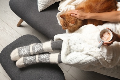 Woman with cute red cat and coffee on grey sofa at home, top view