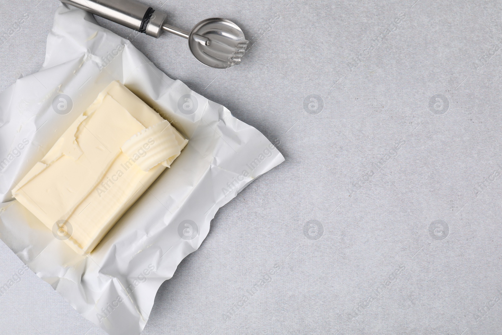 Photo of Tasty butter with curl and spoon on light grey table, top view. Space for text