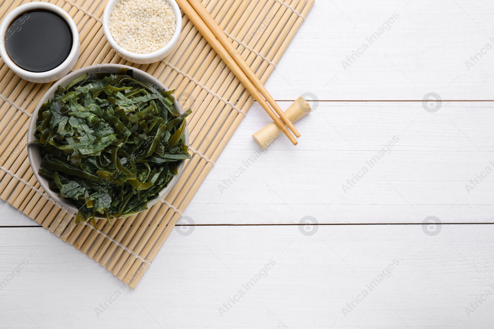 Photo of Fresh laminaria (kelp) seaweed served on white wooden table, flat lay. Space for text