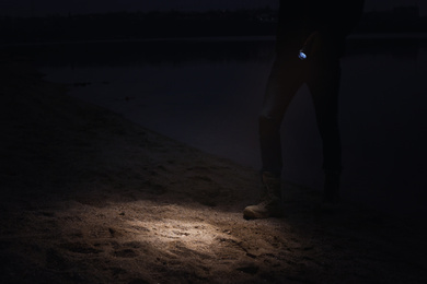Man with flashlight walking near river at night, closeup