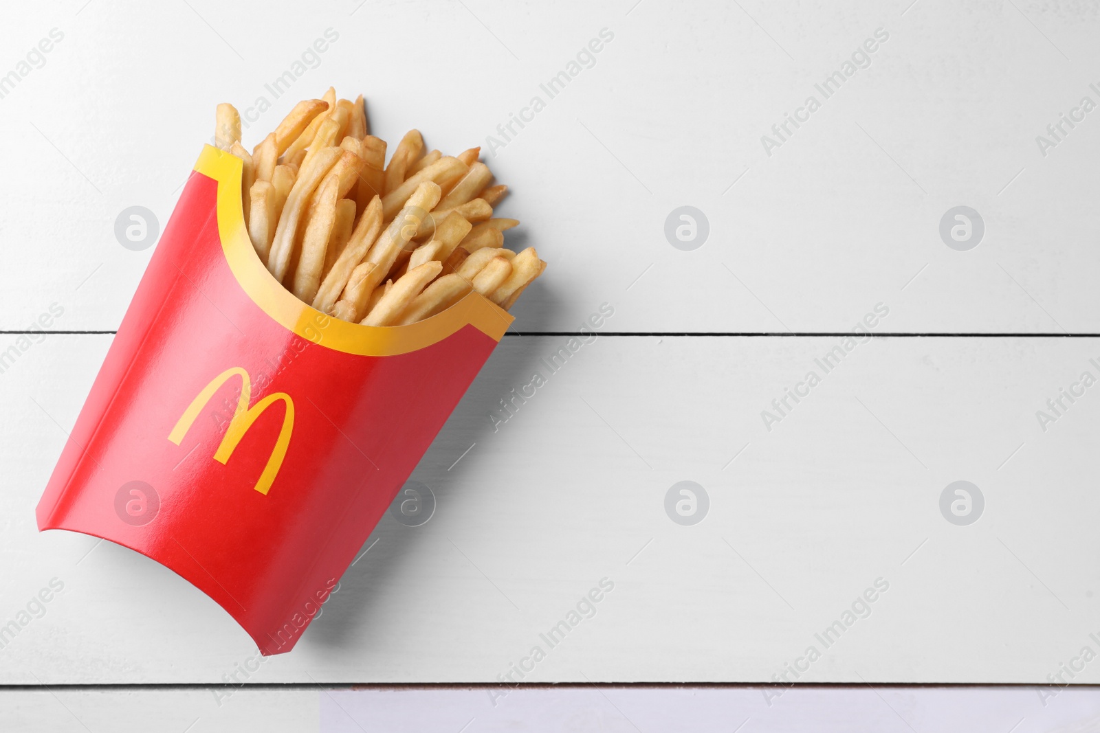 Photo of MYKOLAIV, UKRAINE - AUGUST 12, 2021: Big portion of McDonald's French fries on white wooden table, top view. Space for text