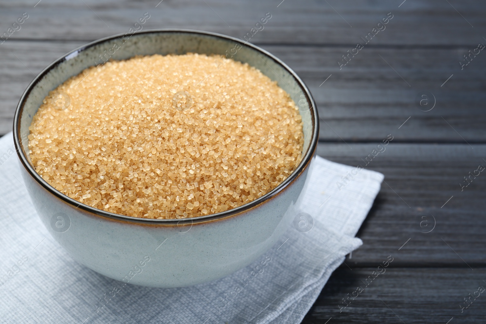 Photo of Brown sugar in bowl on black wooden table, closeup