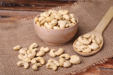 Photo of Tasty cashew nuts in bowl and spoon on table