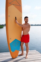 Photo of Man standing near SUP board on pier