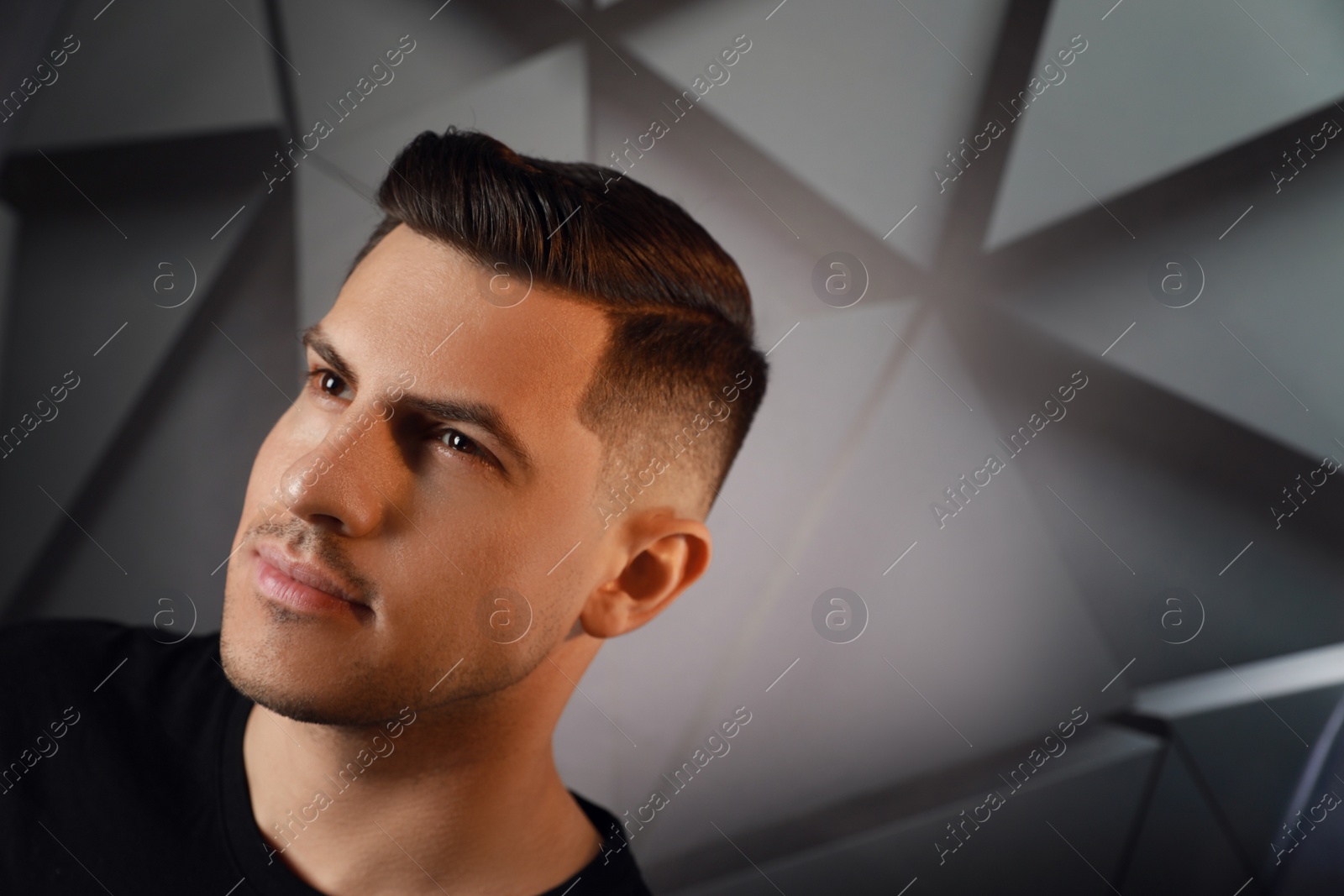 Photo of Handsome man with trendy hairstyle near dark wall, space for text